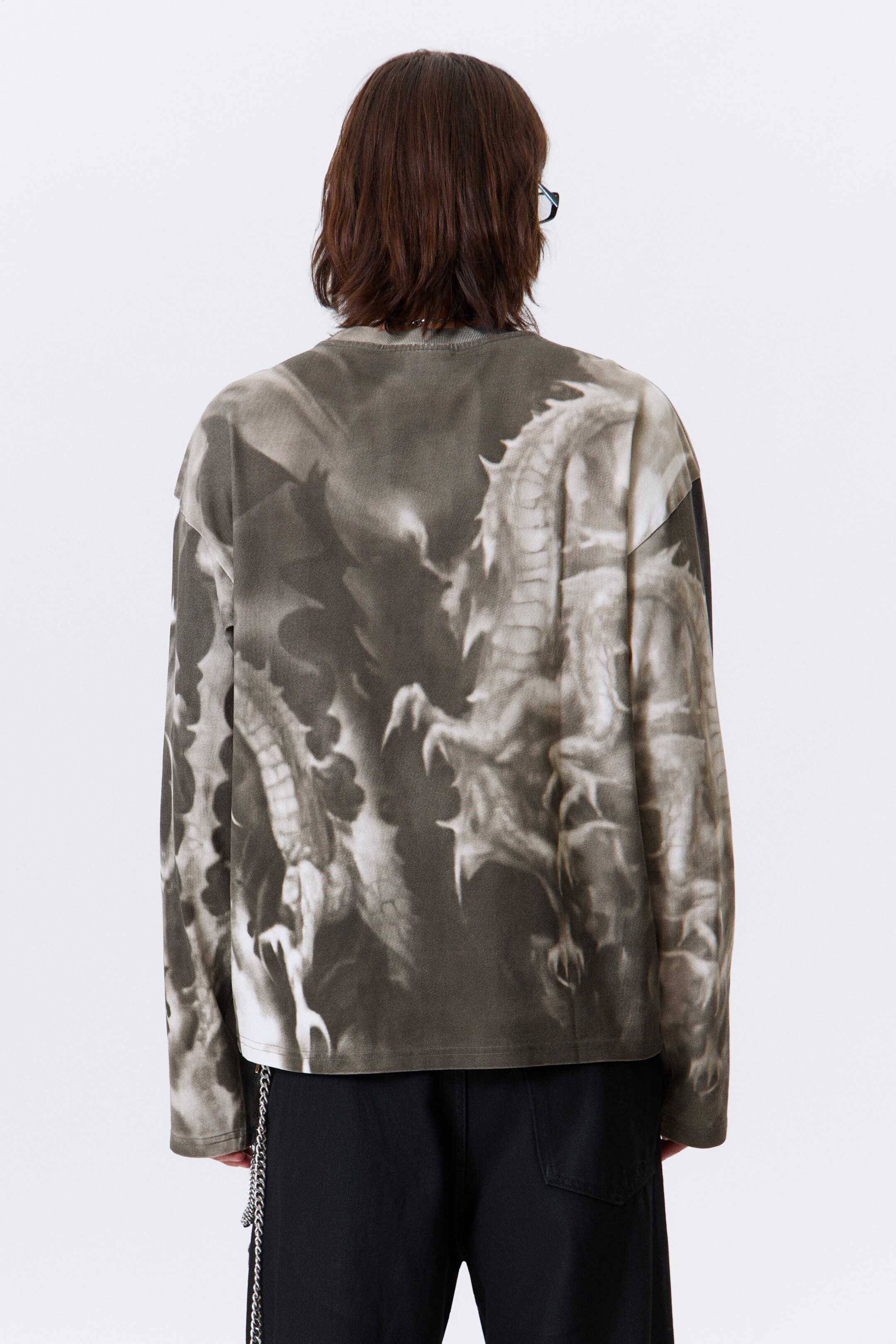 Agrandir l'image: Une chemise à manches longues est présentée de dos, avec un grand graphique détaillé de dragons dans des tons de gris et de brun sur tout le dos et les manches. La chemise présente une coupe ample et un ourlet droit.