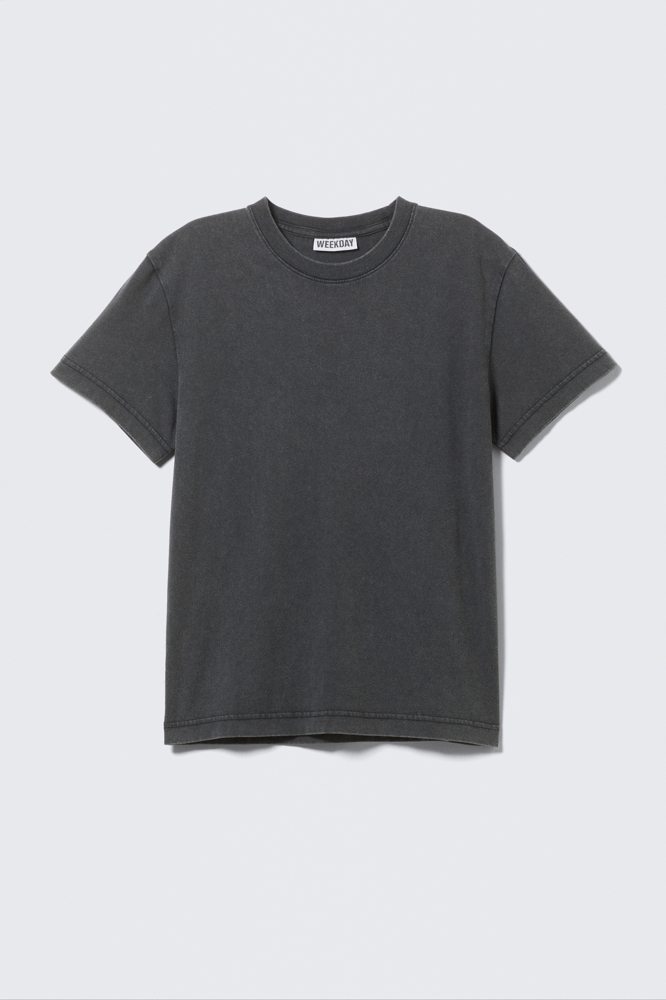 View larger image: A dark gray short-sleeved crewneck T-shirt is being presented FRONT, featuring a snug ribbed neckline and a faded, worn-in appearance. Twin-needle topstitching is visible on the sleeve and bottom hems, and a 'WEEKDAY' label is showing at the back neckline.