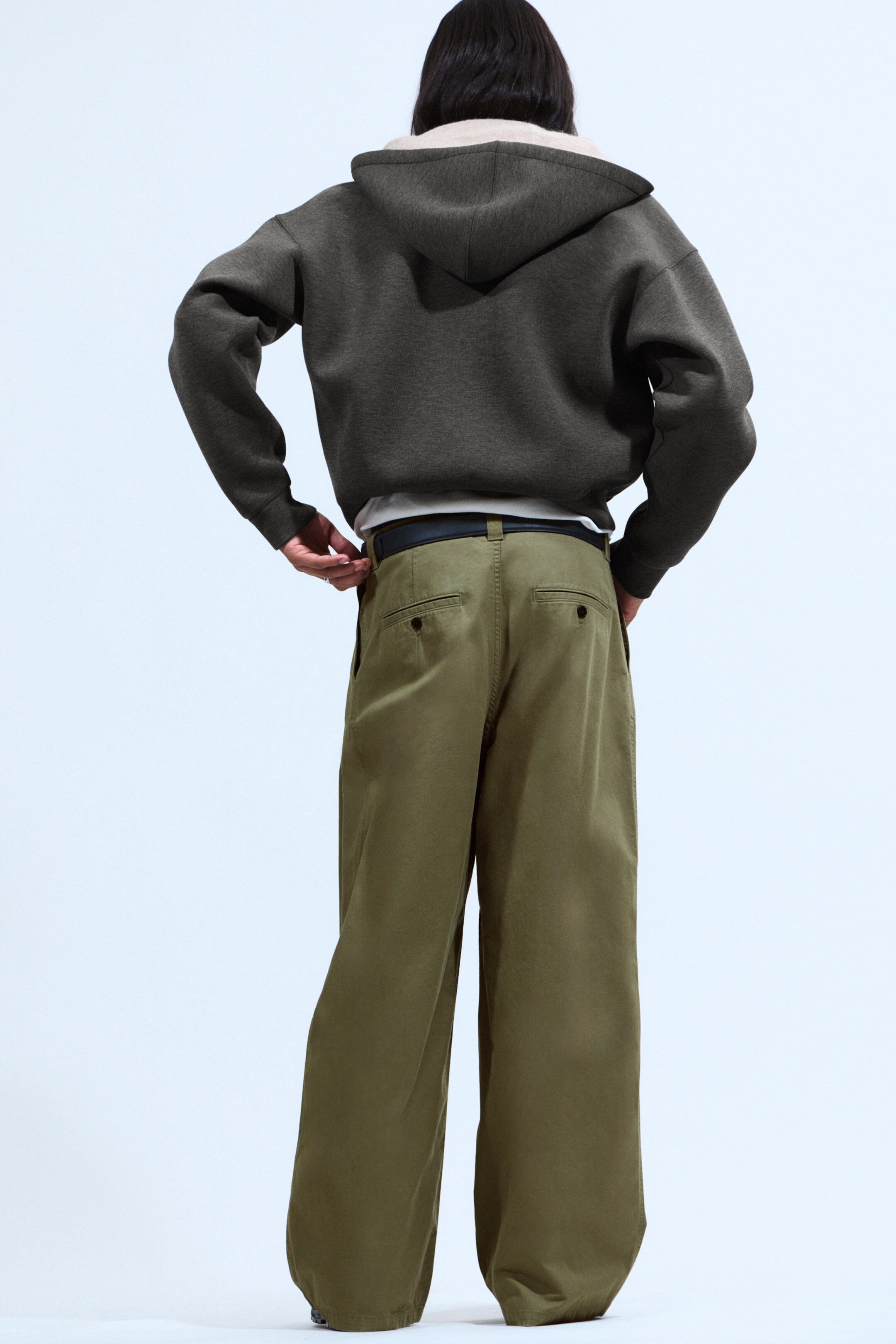 Agrandir l'image: Les chinos olive vert surdimensionnés et amples sont présentés de dos, affichant une silhouette à jambes larges. Ils sont dotés de passants de ceinture avec une ceinture noire, et de deux poches arrière passepoilées avec des détails de renfort.