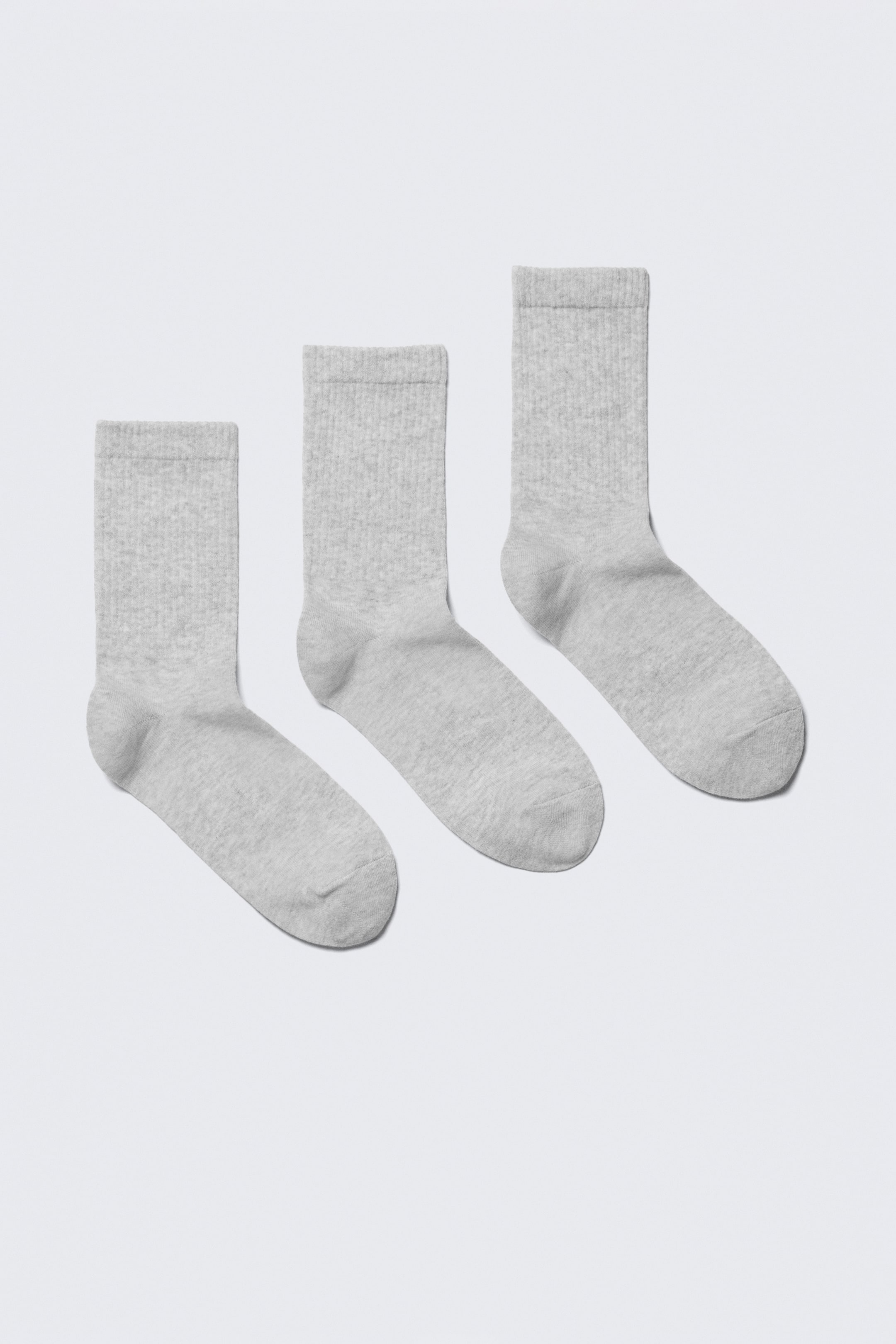 View larger image: Three light grey crew socks are lying flat, arranged diagonally from bottom left to top right. Each sock features a ribbed cuff and a smooth knit body, with their toes pointing towards the bottom left.