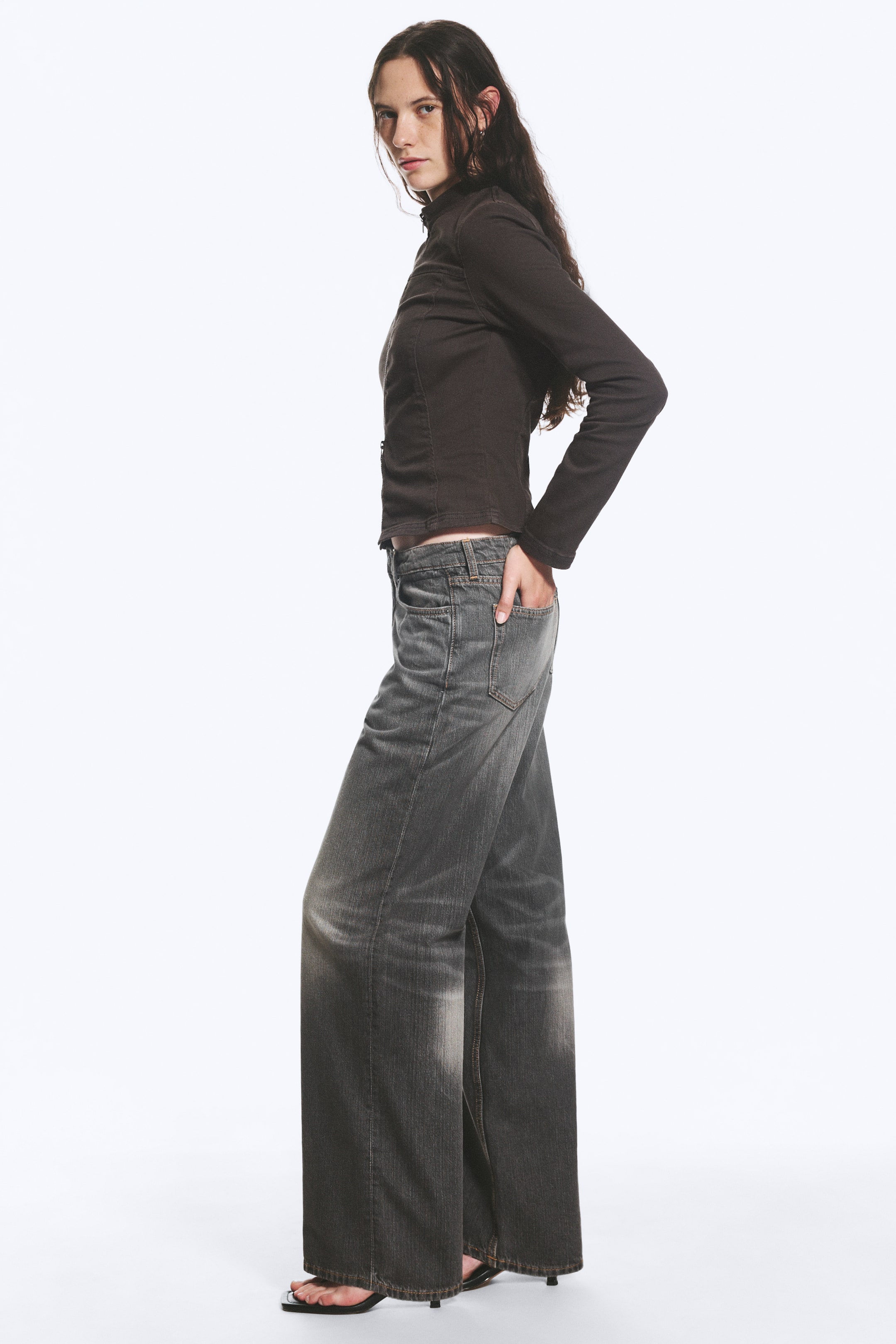 Agrandir l'image: Les jeans à jambes larges sont présentés sous un angle de côté avant, mettant en valeur leur coupe décontractée et leur longueur qui s'étend jusqu'aux pieds. Ils arborent un délavage gris foncé avec des zones plus claires et usées sur les cuisses et le bas des jambes, ainsi que des poches avant visibles et des passants de ceinture.