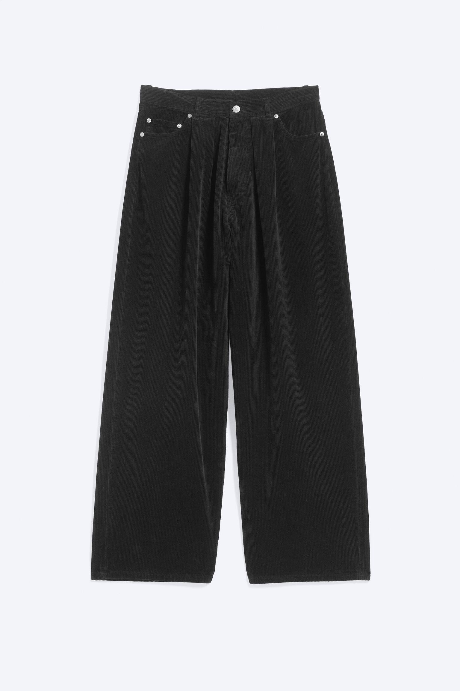 A pair of black corduroy trousers is shown from the front, showcasing a wide-leg silhouette with distinctive front pleats. The trousers feature classic five-pocket styling details, including curved front pockets with silver-tone metal rivets and a central button fastening at the waistband. - 1