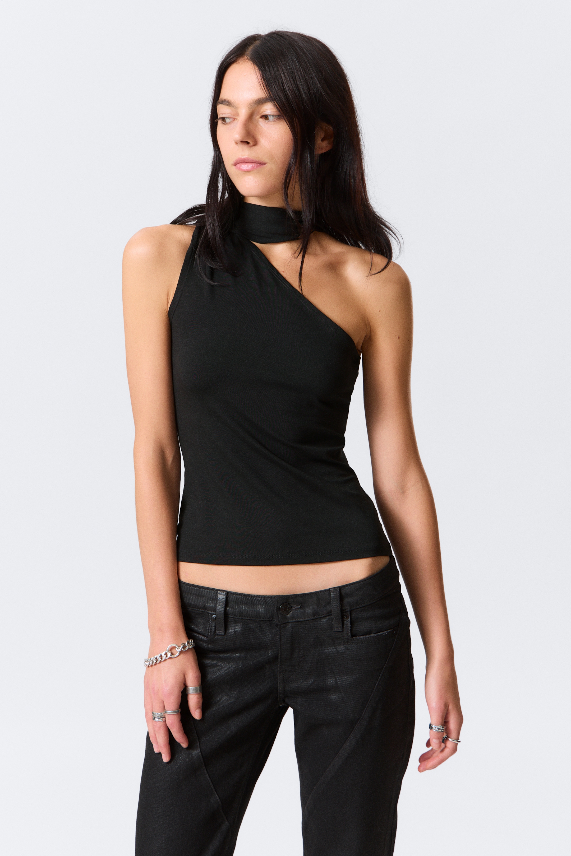 Grotere afbeelding bekijken: Een zwarte one-shoulder top, met een slanke pasvorm en een verstelbare nekband gestyled als een choker, wordt gedragen door het model.