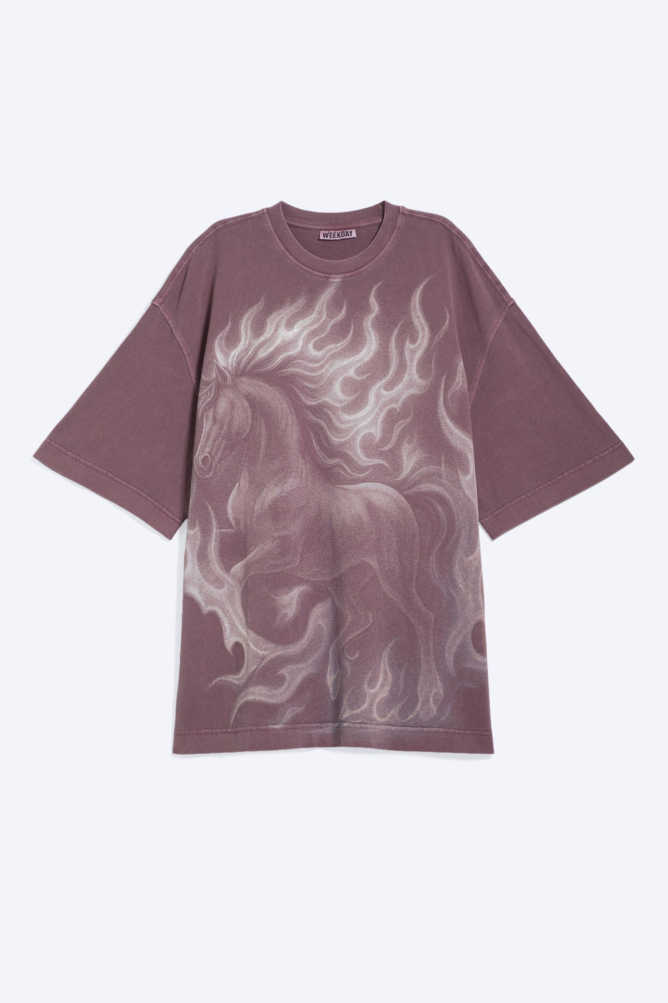 Visualizza immagine più grande: Una t-shirt a maniche corte oversize è mostrata frontalmente, caratterizzata da un colore marrone-violaceo tenue e uno scollo rotondo. Sul davanti è presente una grande stampa di un cavallo in una tonalità più chiara, circondato da motivi simili a fiamme, mentre la t-shirt presenta spalle larghe e cadenti e una vestibilità ampia.