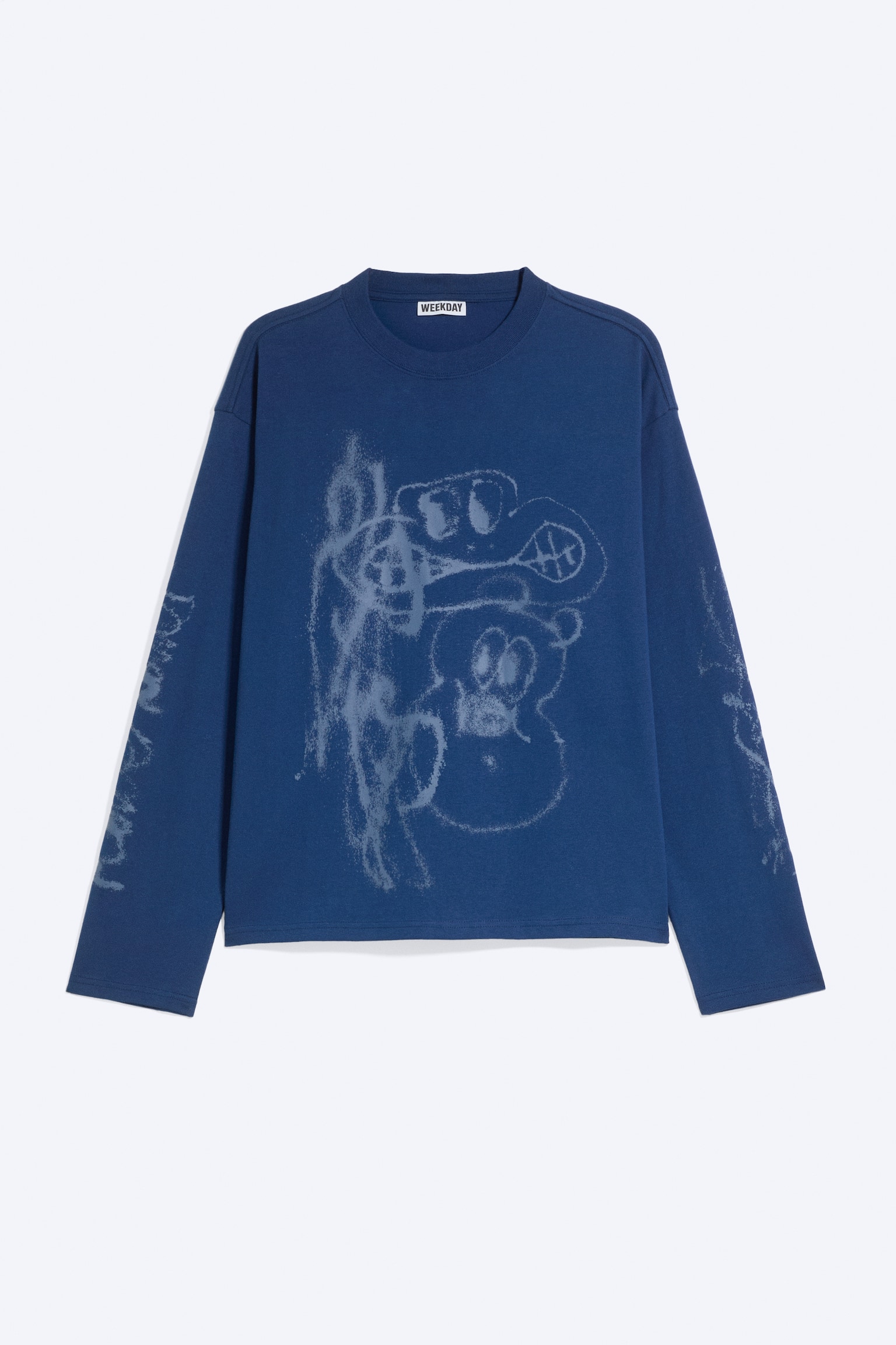 Egy kék, bÅ szabású, hosszú ujjú T-shirt elölrÅl látható, elöl középen egy elhalványult, spray-festett stÃlusú, absztrakt rajzfilmfigurákat ábrázoló grafika dÃszÃti a mellrészen. A T-shirt ujain további elhalványult grafikai részletek, bordázott, kerek nyakkivágás, valamint dupla varrással készült alsó szélek láthatók.