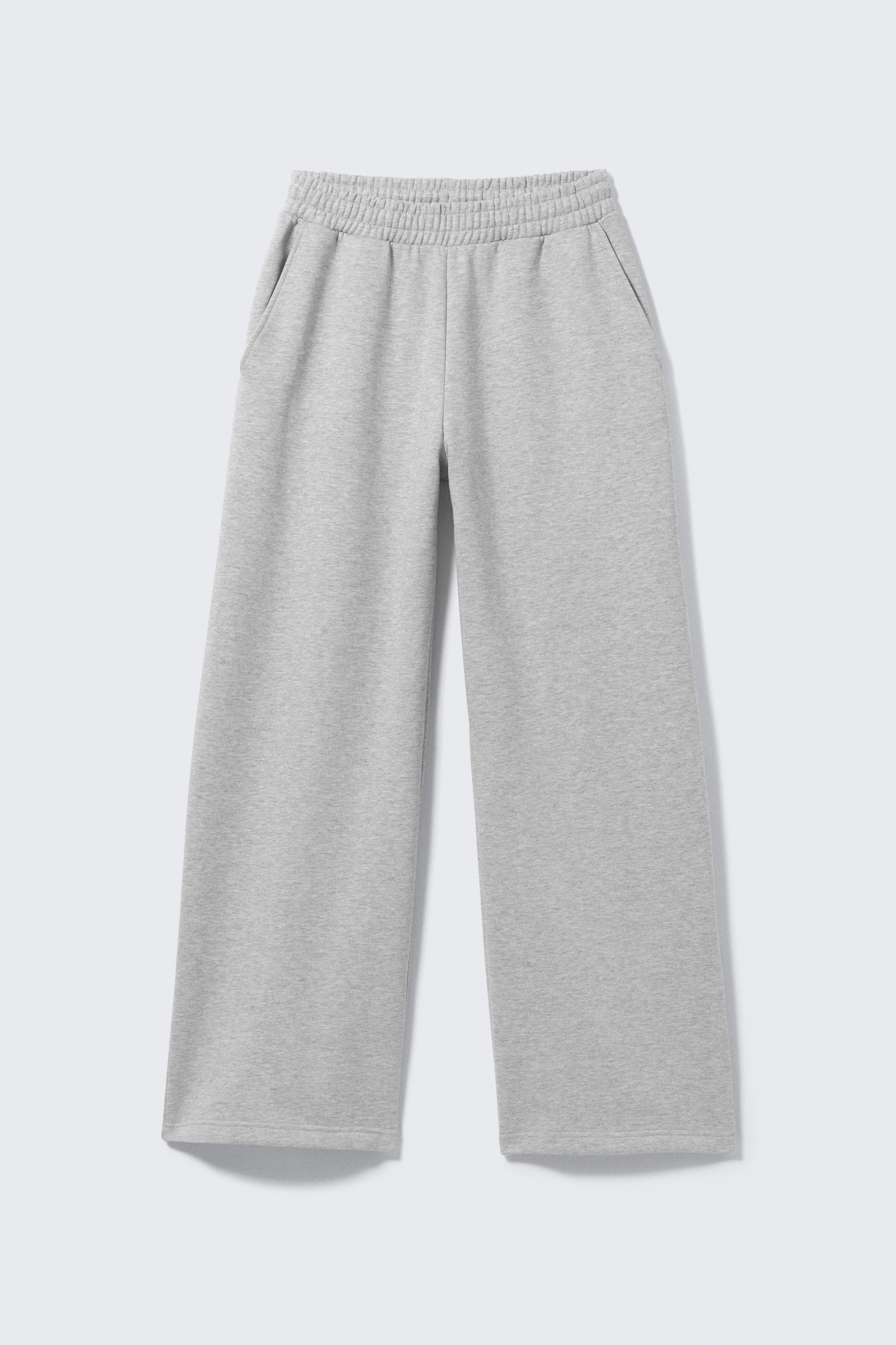 Grösseres Bild ansehen: Ein Paar hellgraue Jogginghosen zeigt seine FRONT-Ansicht. Ein breiter, geraffter elastischer Bund ist oben zu sehen. Zwei schräg angesetzte Seitentaschen sind sichtbar, und die Jogginghose hat gerade, weite Beine mit einfachen Säumen.