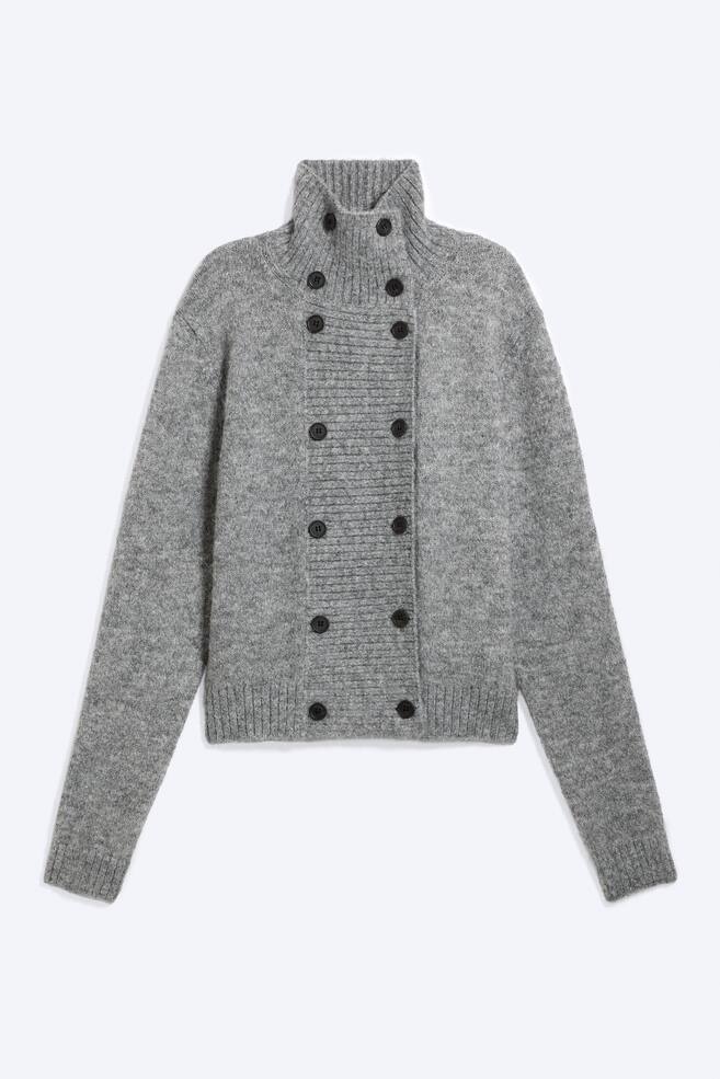Een dubbelrijige cardigan met knopen in een grijs gemÃªleerde knit wordt van voren getoond, met een hoge geribde kol met tunnelhals en twee parallelle rijen donkere knopen langs een geribd voorpand. Het langÃ¤rmelige breigoed heeft geribde boorden aan de mouwen en een bijpassende geribde zoom. - 1