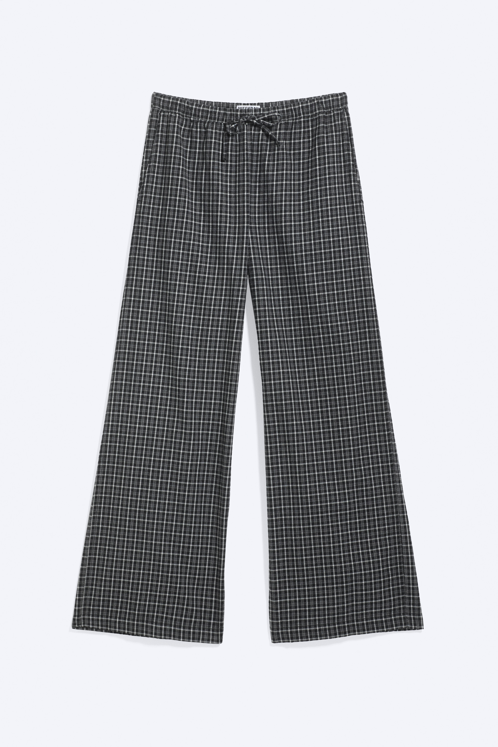 Das Model trÃ¤gt eine weit geschnittene Flanell-Pyjamahose mit schwarz-weiÃem Karomuster. Die Hose verfÃ¼gt Ã¼ber einen mittelhohen, elastischen Bund mit Kordelzug und wird mit einem hellblauen Langarmshirt kombiniert.