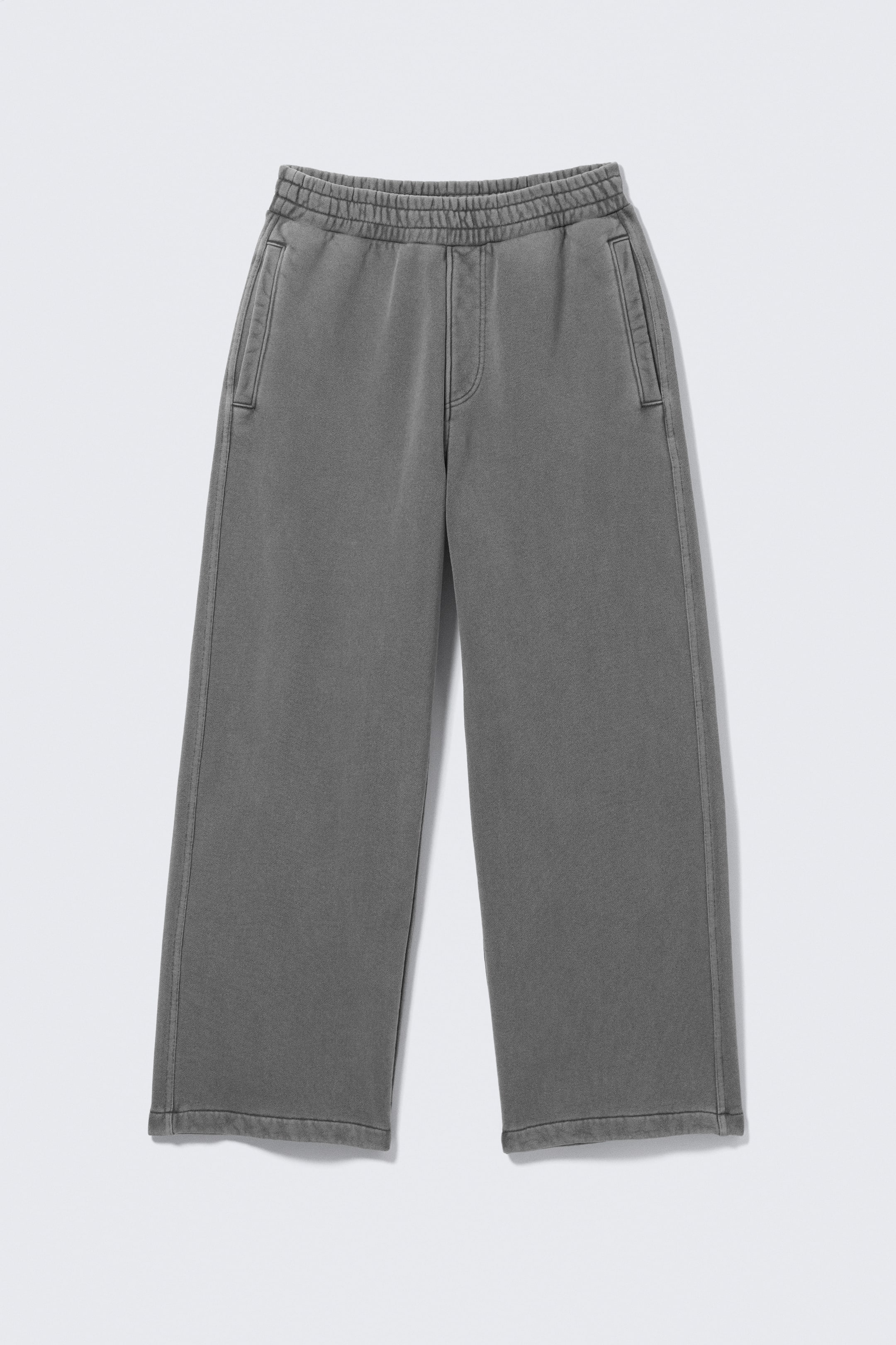 View larger image: The FRONT of a pair of dark grey, washed-effect joggers features an elasticated waistband and two vertical side pockets. The trousers present wide, straight legs with plain hems.