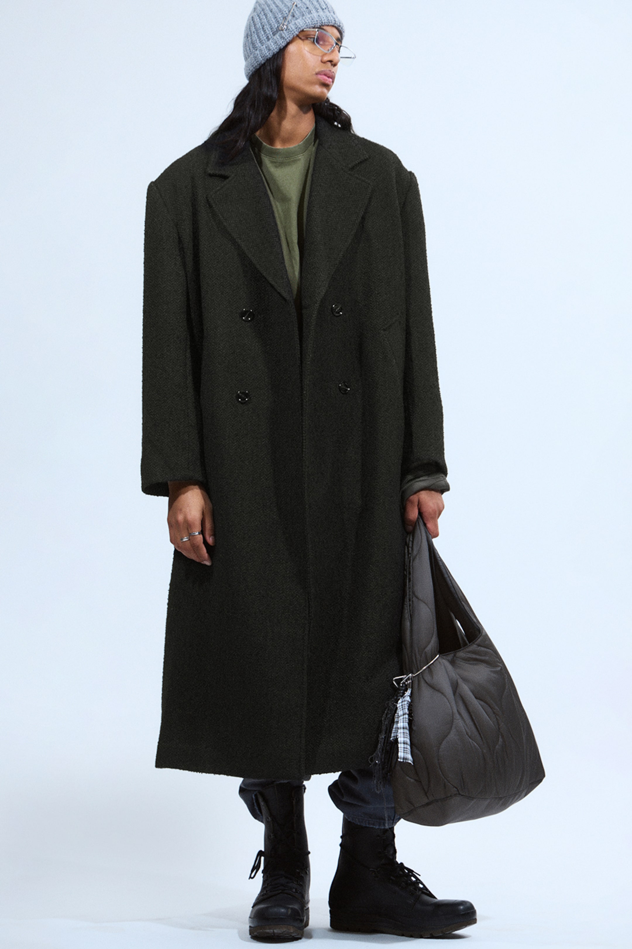 Model wearing a black oversized herringbone coat and a grey beanie