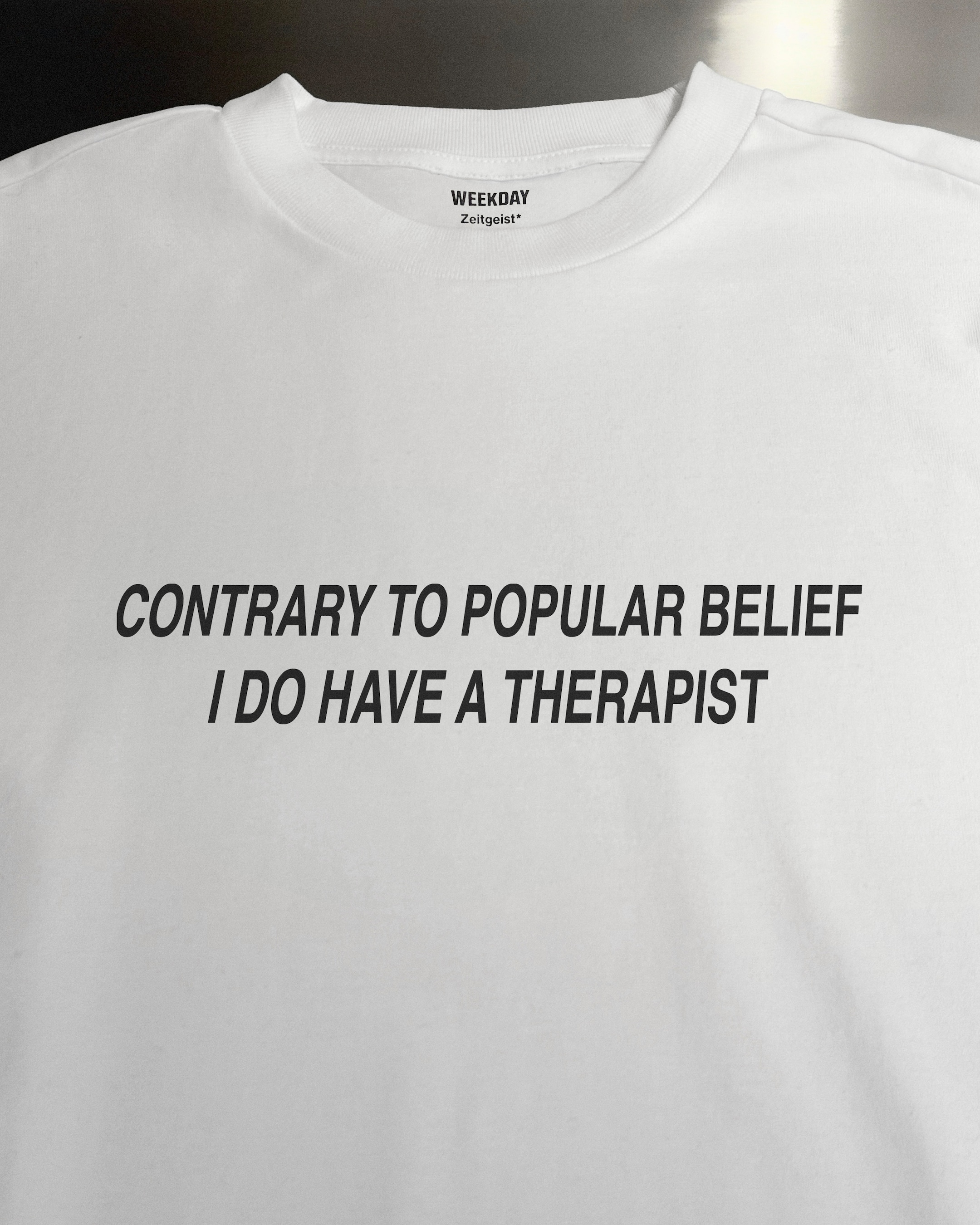 A person wearing a printed white Zeitgeist t-shirt saying “Sorry I missed your call. I was watching it ring till it stopped.”