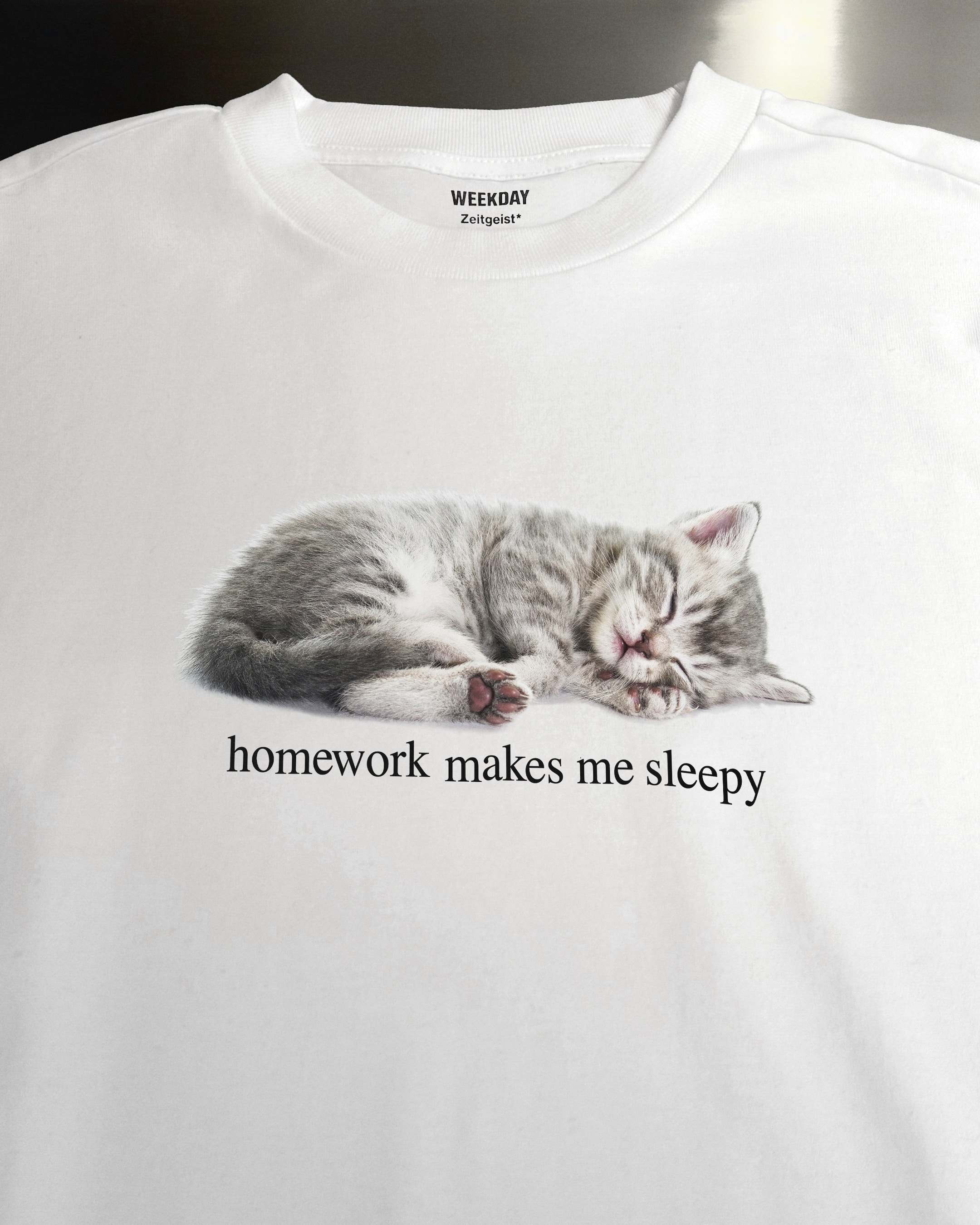 A person wearing a printed white Zeitgeist t-shirt saying “Sorry I missed your call. I was watching it ring till it stopped.”