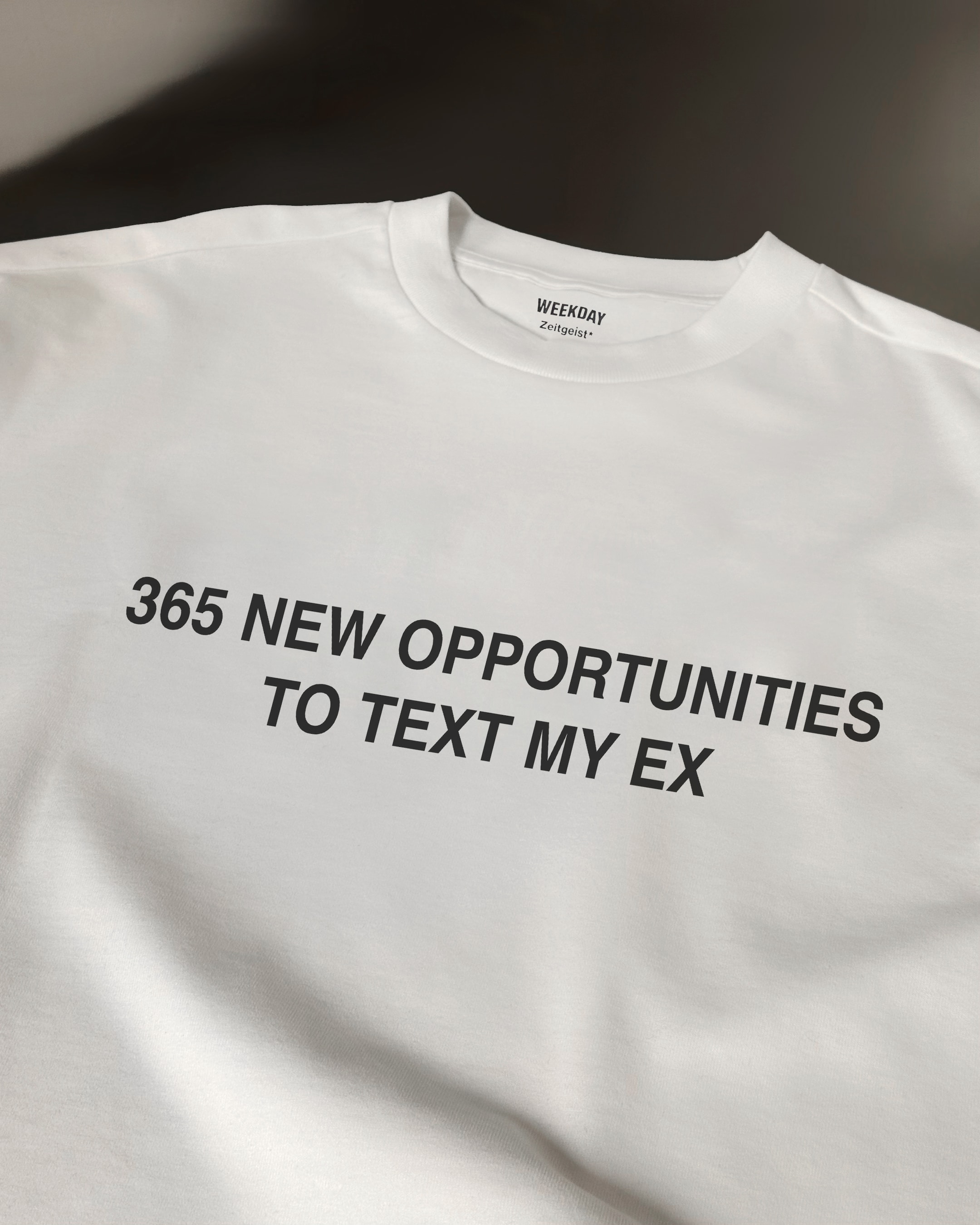 A person wearing a printed white Zeitgeist t-shirt saying “Sorry I missed your call. I was watching it ring till it stopped.”