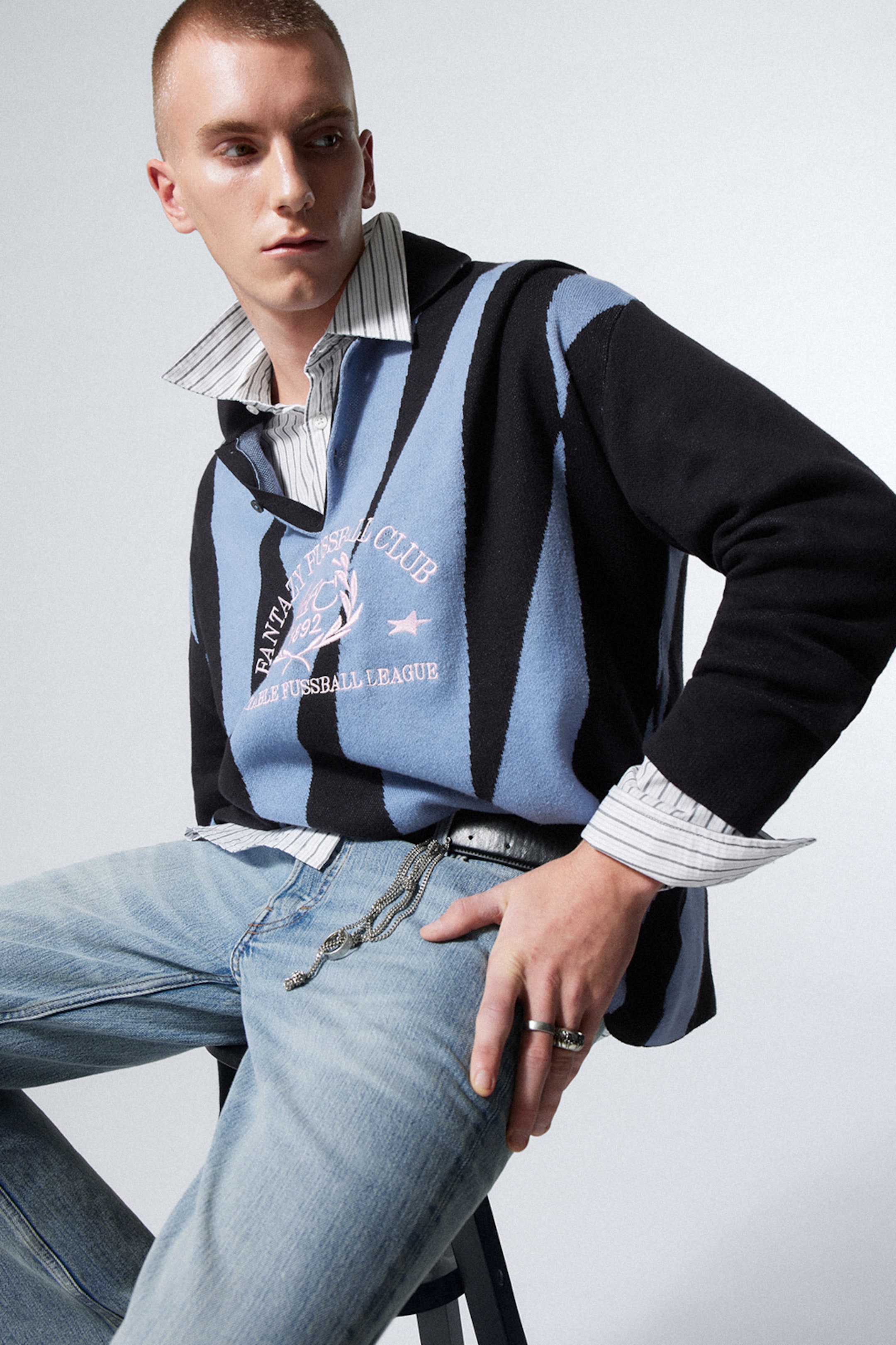 Model posing on a stool while wearing a pair of blue weekday jeans and a graphic polo sweater