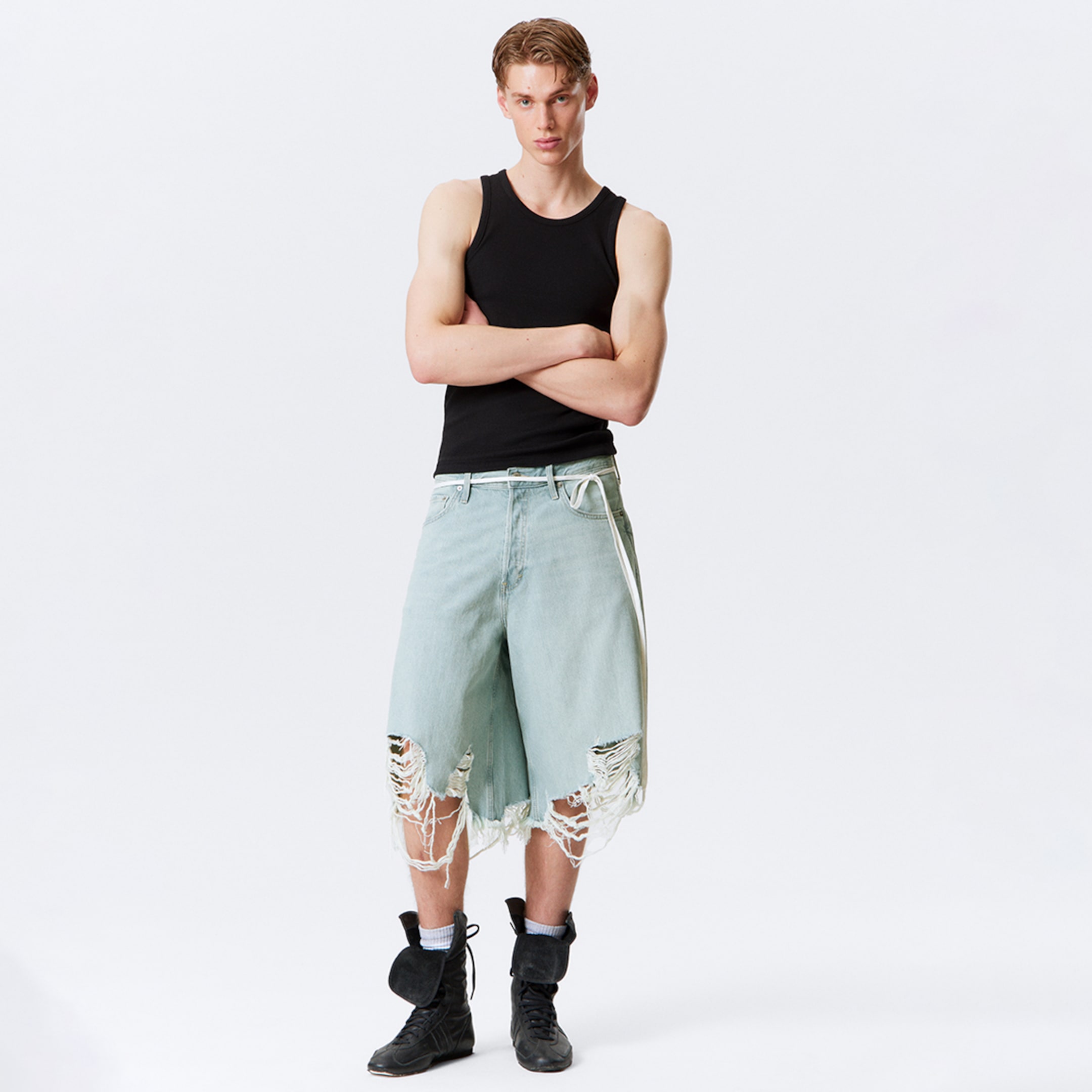 Model wearing a black tank top together with a pair of distressed denim jorts