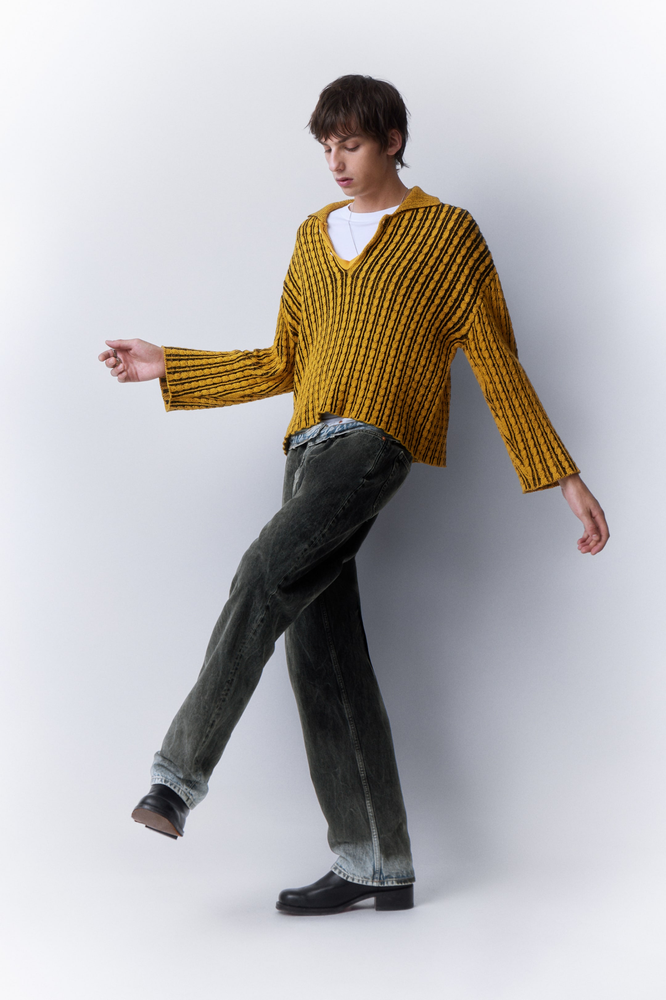 Model wearing a yellow & black knitted polo together with a pair of grey/black weekday jeans