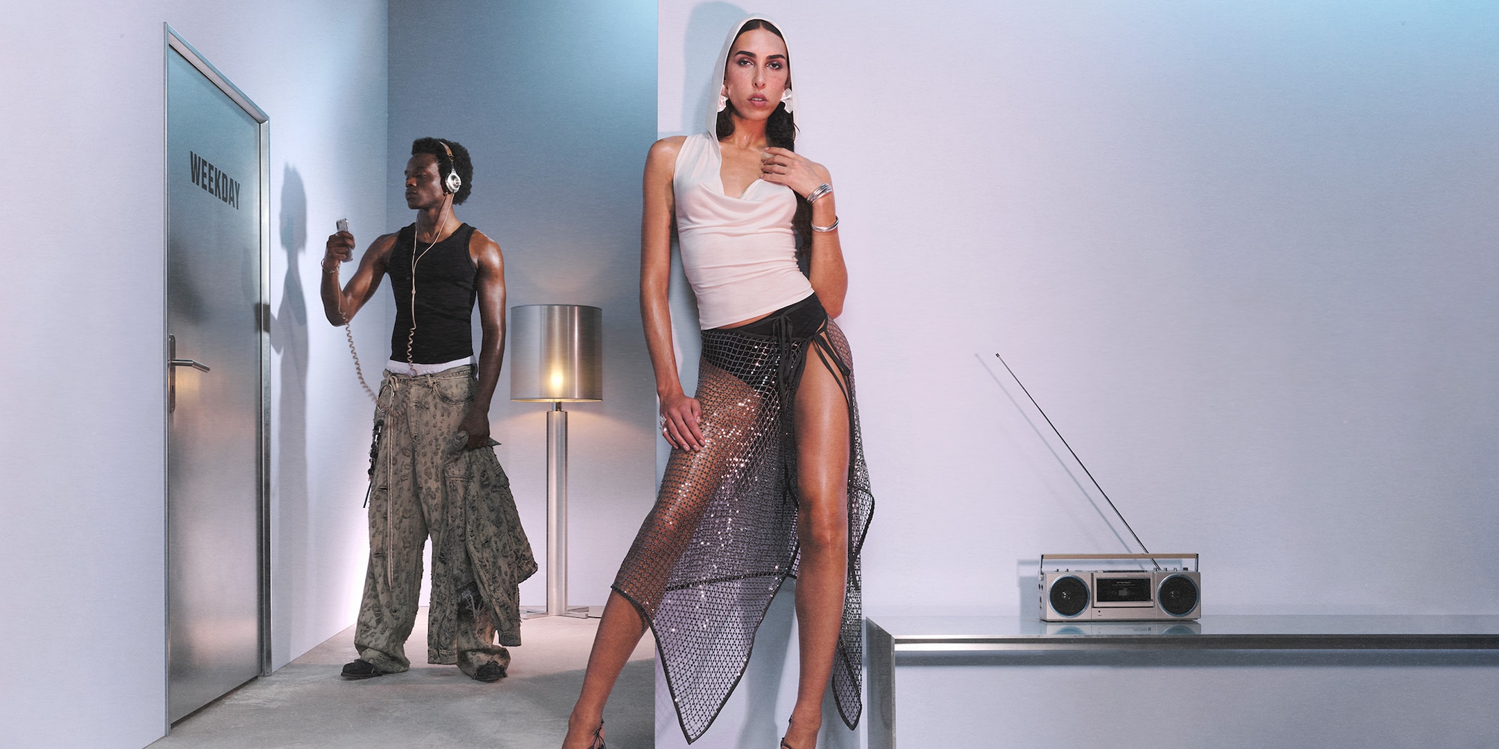 Raya Martigny in a white sleeveless hooded top and grey sparkly wrap skirt. Jolagreen23 in black tank top and beige distressed Astro jeans.